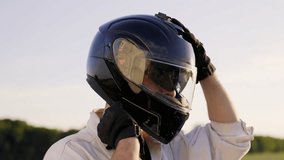 The motorcyclist is sitting on the motorcycle and putting on a helmet. The man is in the middle of a field at sunset. - Powered by Shutterstock - Get 15% off with code: PIKWIZARD15