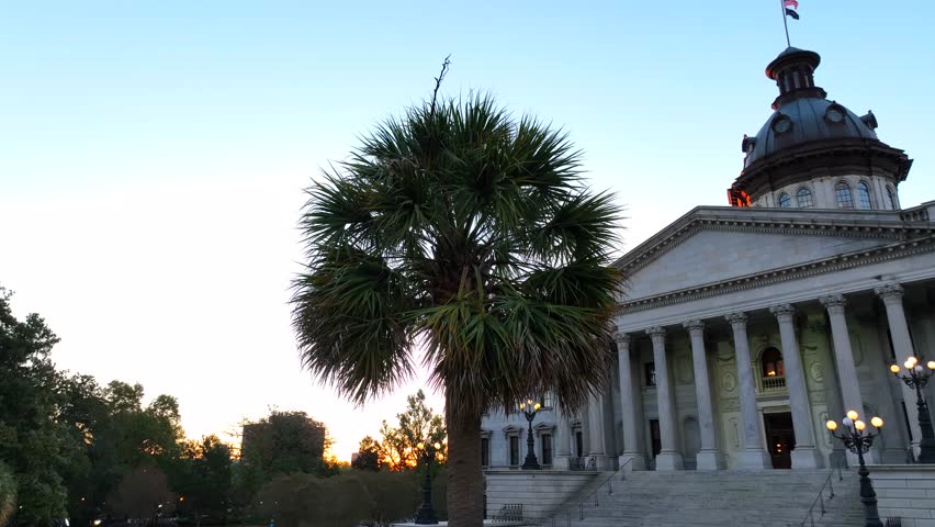 Palm tree with South Carolina State House during sunrise. Aerial establishing shot in Columbia, the capital city of SC.