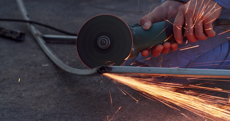 Blacksmith performing welding repair work using professional equipment. Blacksmith cutting metal using angle grinder while working in industrial workshop, man cuts rusty metal beam using round turbine