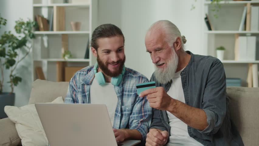 Young adult assists elderly man with online shopping via app, using bank card for secure payment, enhancing digital literacy, cross-generational tech education, bridging digital divide - Powered by Shutterstock - Get 15% off with code: PIKWIZARD15