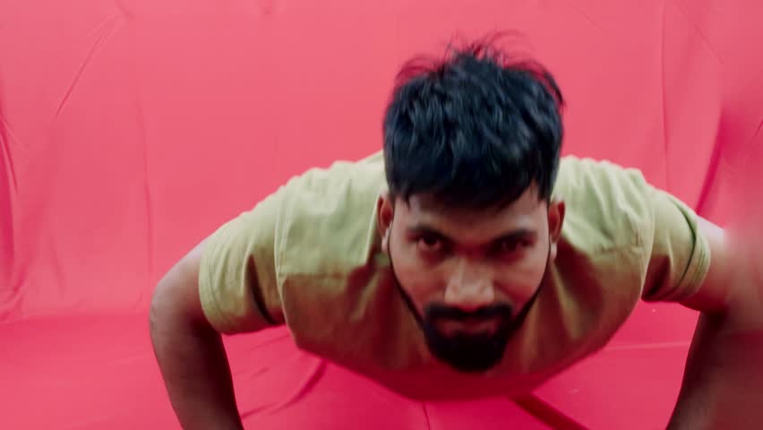 Man with beard in casual clothing doing push up gesture against a vibrant red background asian male