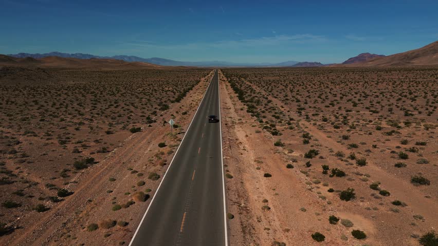 Black car driving on desert highway in Nevada. Empty street to nowhere. Road from above in the dry hot Wild West America landscape. Aerial drone