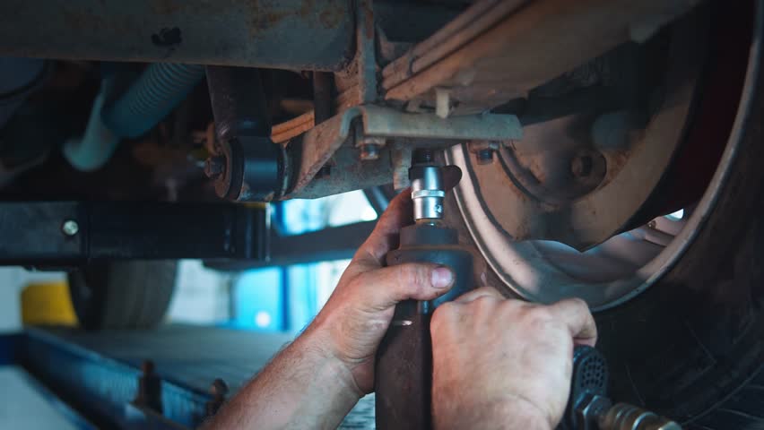 Repairman inspects and tunes car's undercarriage and tire using tools on lift platform in service bay. Royalty-Free Stock Footage #3422530527