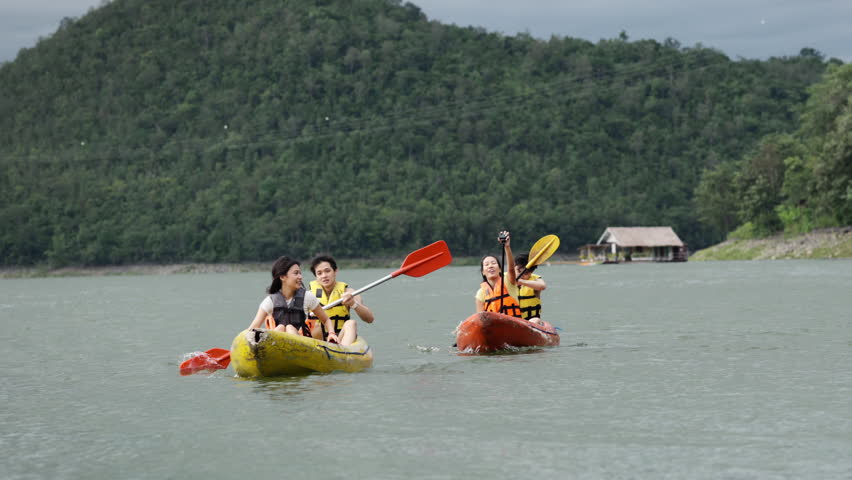 Group of Young Asian man and woman friends with life vest kayaking together in the lake. Happy generation z people enjoy and fun outdoor lifestyle travel nature lake house on summer holiday vacation.