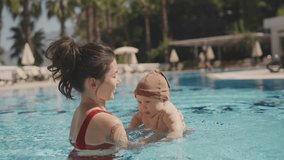 Happy baby at the swimming pool splashing water in slow-motion. Mother holding infant son. Beautiful woman mom teach to swim little baby boy, laugh and smile. Soft touch, love care, summer vacation - Powered by Shutterstock - Get 15% off with code: PIKWIZARD15