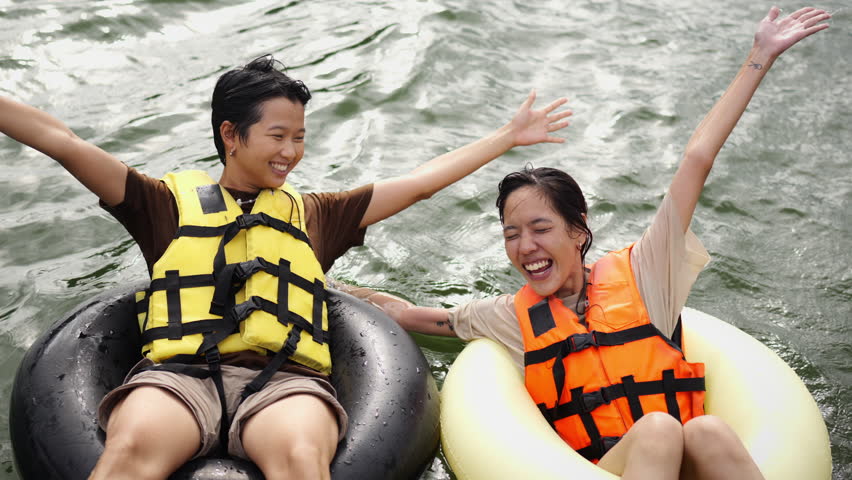 Young Asian woman friends with life vest and swim ring playing water together in the lake. Happy generation z people enjoy and fun outdoor lifestyle travel nature lake house on summer holiday vacation