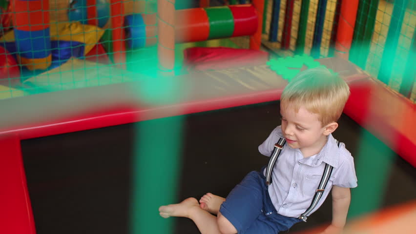 Small blond boy of three years, jumping on a trampoline and falls on the ass, slow motion.