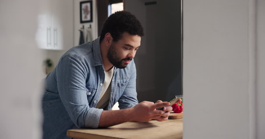 Happy man, phone and typing in kitchen for social media, networking or communication at home. Young male person smile on mobile smartphone for online chatting, texting or research on table at house