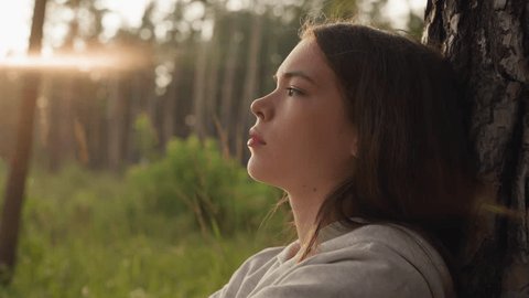 Tired woman leans against tree in forest at sunset. Young lady feels negative emotions after hard breakup finding solace from stress in nature Stock Video
