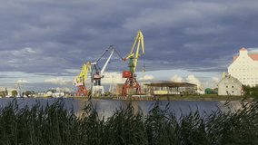 Panning shot of cranes and buildings against cloudy sky at cargo port in Kaliningrad, Russia