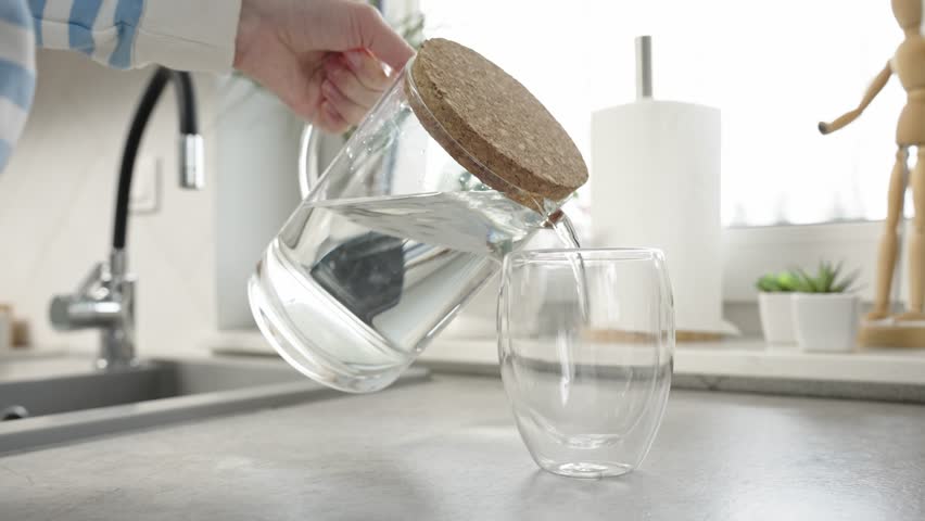 Woman pouring fresh pure water from jug into glass in kitchen, Quenching thirst, Lifestyle healthcare concept