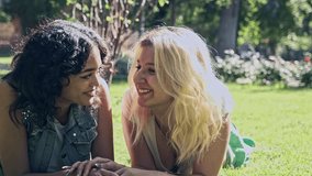 Slow motion video of two young lesbian girls holding hands lying on the grass smiling looking at each other