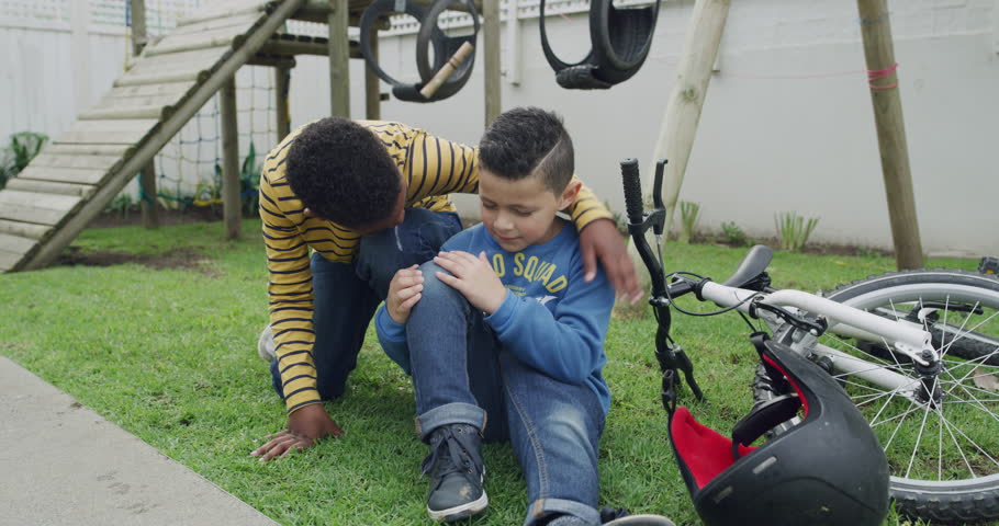 Bike accident, injury and boy friends on playground together after mistake for support, care or comfort. Kids, pain or fall with a male child and best friend on grass for bicycle riding at school