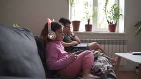 Child girl 5 years old playing video games on the sofa while father working with laptop 
