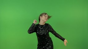 A young girl in a black shiny dress, dancing and singing. Cheerfully jumps and rejoices. On a green background.