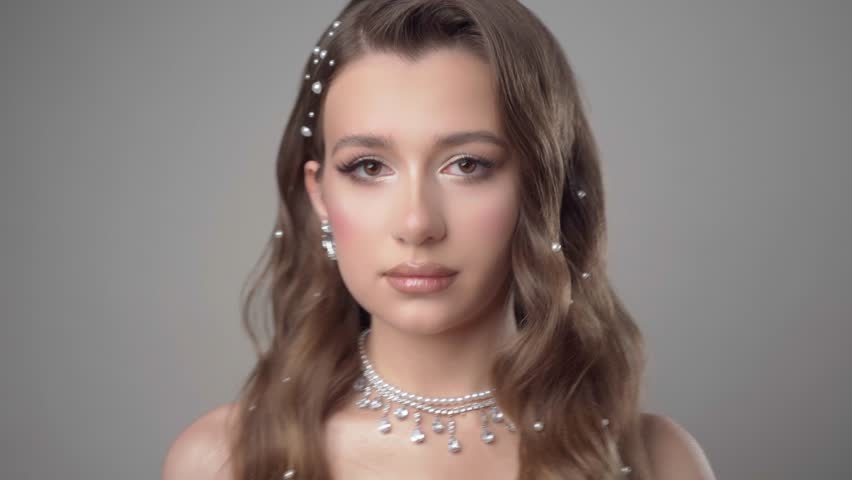 Portrait of a young beautiful female model with evening makeup, diamond necklace, ring, earrings and hairstyle Hollywood Wave, decorated with pearls, posing in the studio on a white background.