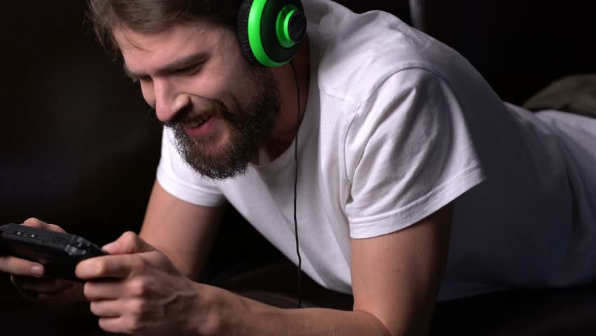 The man is lying on the couch and is playing in the console