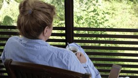 A young Caucasian woman, 40 years old, drinks morning coffee on the terrace. Holidays at the dacha.