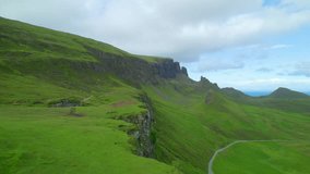 AERIAL: Green grassy slope of The Quiraing intersected by steep rocky cliffs, formed by a massive landslip at the northern part of Trotternish Ridge on Isle of Skye. Beautiful and dramatic landscape.