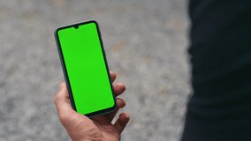 Closeup finger touching green smartphone screen. Hand holding mockup cell device on street. Unrecognized businessman scrolling chroma key mobile phone checking online chat. Application user concept - Powered by Shutterstock - Get 15% off with code: PIKWIZARD15