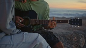Tattooed man hands playing guitar at sunset closeup. Romantic young woman bonding to curly boyfriend listening serenade at evening. Love couple dating at ocean coast horizon. Togetherness concept - Powered by Shutterstock - Get 15% off with code: PIKWIZARD15