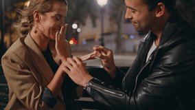 Man put engagement ring kissing girlfriend hand. Loving boyfriend proposing on evening date. Attractive smiling woman rejoicing admiring diamond. Happy couple enjoy intimate moment in night city park - Powered by Shutterstock - Get 15% off with code: PIKWIZARD15