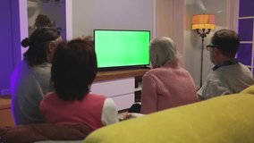 Family watching TV. Green screen. A young man, a mature woman, a grandmother and an elderly man are sitting on the sofa and watching TV. A young man hands the TV remote control to an older man.
