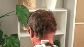 A wife cuts her elderly husband hair at home. Cutting mens gray hair with a clipper.