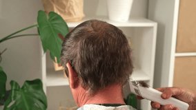 A wife cuts her elderly husband hair at home. Cutting mens gray hair with a clipper.