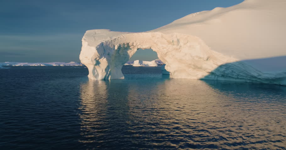 Drone flight into big glacier arch in Antarctica. Huge hole in melting iceberg, ocean water, polar nature environment. Arctic winter landscape, global warming problem. Climate change, sunny winter day