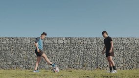 Two young sportive girls juggling soccer ball and kicking it to each other while exercising on green lawn by stone wall on a sunny day with cloudless sky - Powered by Shutterstock - Get 15% off with code: PIKWIZARD15