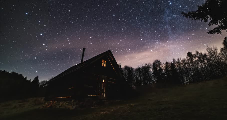 Romantic night sky with milky way stars over old wooden hut in forest nature astronomy time lapse