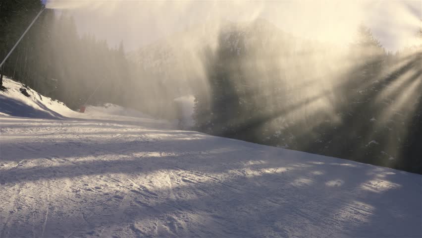 Skier skiing trough misty clouds of fresh snow from snow cannon in winter ski resort, holiday sports recreation