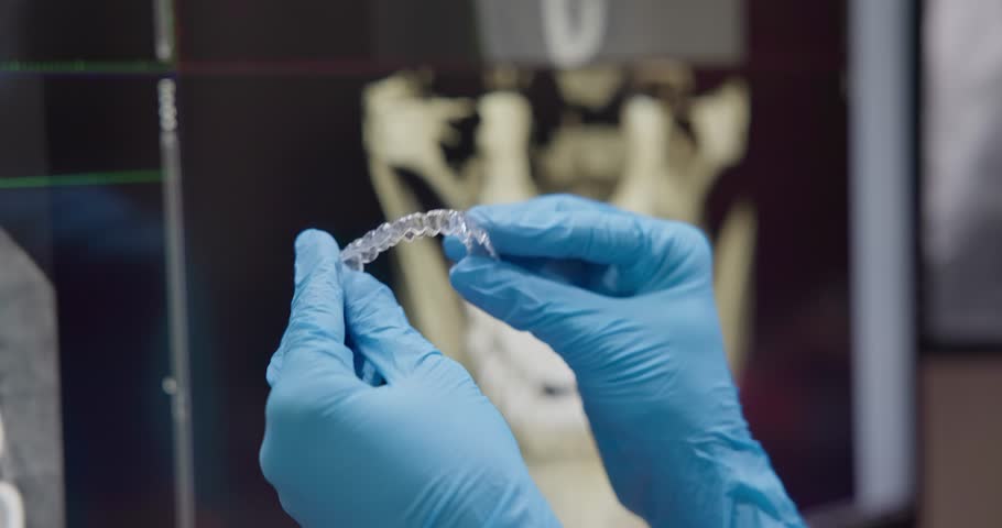 Orthopedic dentist doctor holds night bruxism protection muscle relaxant mouth guard or Plastic aligner Brace on x-ray background