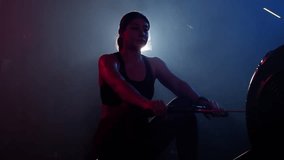 In the gym, a woman trains on a rowing machine, surrounded by a mystical mix of blue and red lights and a hint of fog - Powered by Shutterstock - Get 15% off with code: PIKWIZARD15