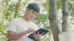 Young Asian man standing under trees using digital tablet and smartpen drawing plan, searching information online, paperless concept, soft files transfer, online transactions digital drawing - Powered by Shutterstock - Get 15% off with code: PIKWIZARD15