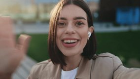 POV Webcam View of Charming Girl Waving, Talking on Video Call Using Smartphone While Standing in Park. Smiling Brunette Lady in Brown Trench Having Online Conversation with Friend or Colleague