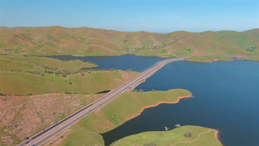 State Route 152 On San Luis Reservoir Surrounded With Lush Green Hills In California, USA. aerial shot