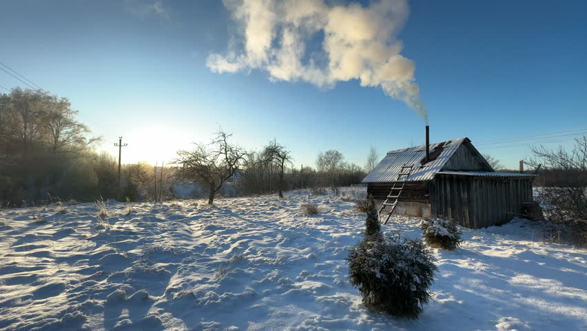 Bathhouse in village in winter time. Smoke from a bathhouse chimney in village. Russian Bath House in countryside. Wooden home in rural in winter. Smoke from Country houses chimney in countryside.