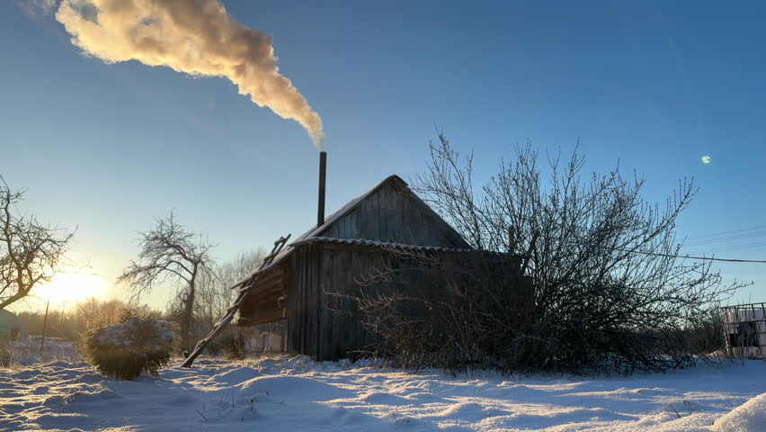 Bathhouse in village in winter. Smoke from a bathhouse chimney in village. Russian Bath House in countryside. Wooden home in rural in winter. Smoke from Country houses chimney in countryside. Banya