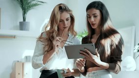 Video of two attractive young business women working with the digital tablet while talking in a modern office
