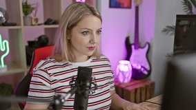Cheerful blonde streamer girl having a blast, pointing a finger at you through the camera! enjoying a cracking gaming night in her cozy room, spreading happy vibes.