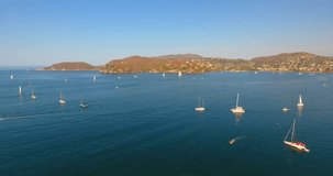 Panning over a bay filled with a regatta of sailing vessels and yachts offshore from Zihuatanejo, Mexico