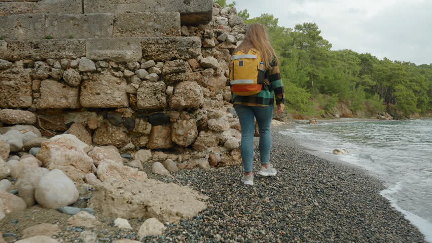 Young woman makes her way along the stone wall of an ancient building, and the waves almost touch its walls. Royalty-Free Stock Footage #3424104171