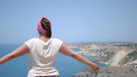 The girl stands on the edge of the summit near the sea and enjoys freedom and life. HD, 1920x1080, slow motion