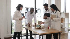Handsome middle aged African American doctor, anatomy teacher, explaining bones anatomy using skeleton model for diverse students in white coats. Medicine, education, anatomy concept. - Powered by Shutterstock - Get 15% off with code: PIKWIZARD15