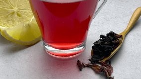 Red hibiscus tea in a glass cup and dried hibiscus flowers on the table

