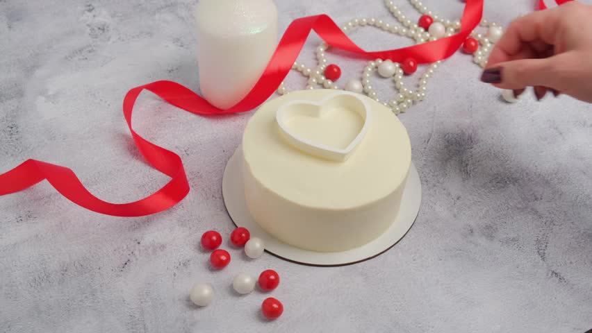 A pastry chef decorates a cake with red heart-shaped cream for Valentine