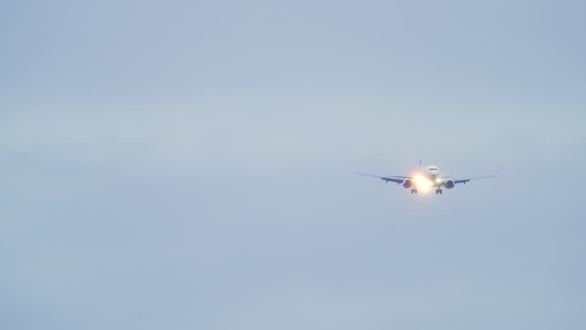 Front view flying jet passenger plane. Scenic shot airliner arriving in airport and landing at dusk. Travel by air transport. Slow motion