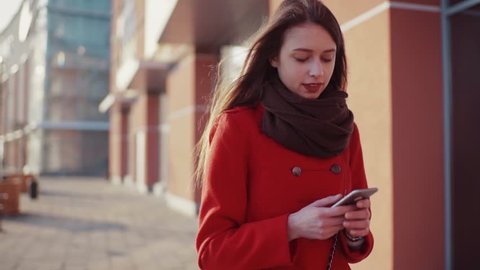 Adorable young woman in a stylish look walks down the street, takes her phone, dials the number, cheerfully talks via her smartphone. Modern technologies, communication, positive emotions.